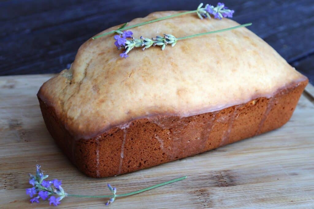 A loaf of glazed lavender with fresh lavender stems sits on a board.