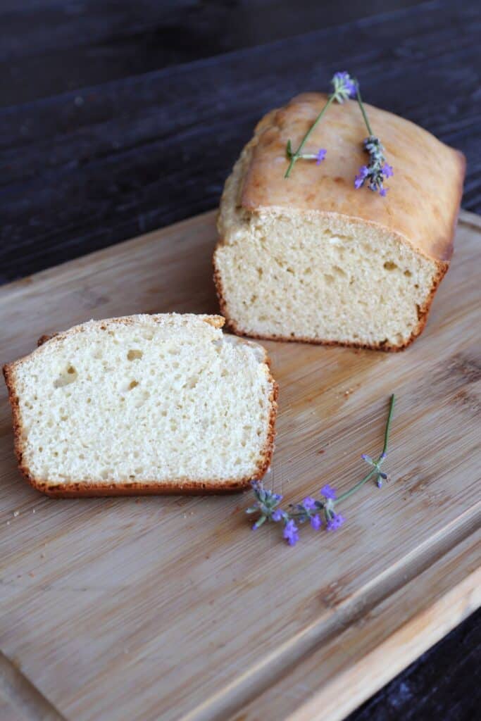 Slices of bread on a board with remaining loaf behind them. Fresh lavender flowers sit on the board and loaf.