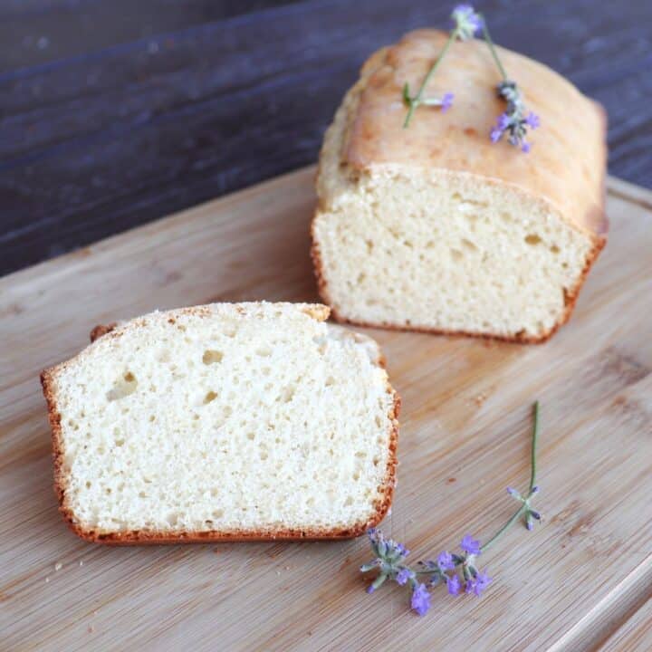 A slice of bread on a cutting board with remaining loaf in the background and stems of fresh lavender surrounding them.