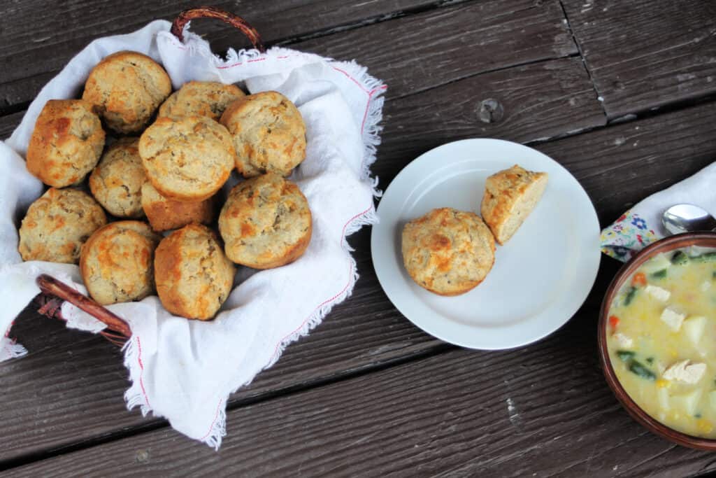 A table set with a basket of muffins, a plate with a muffin cut in half and a bowl of creamy soup as seen from above.