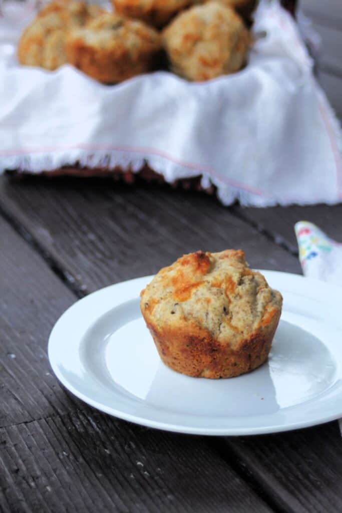 A cheddar rye muffin on a plate with a basket full of more muffins in the background.