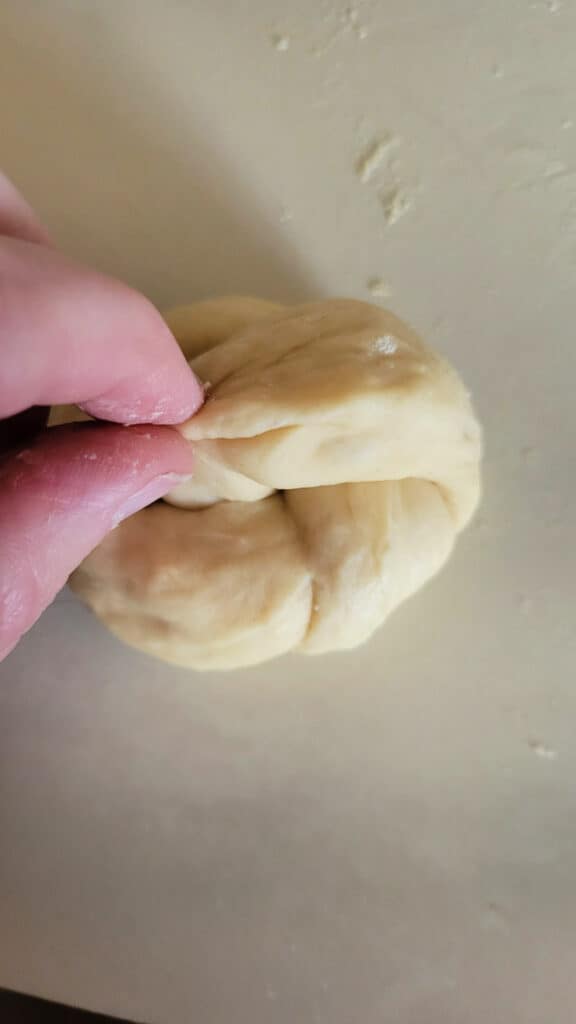 A woman's fingers pinching together the ends of bread dough to make a knotted roll.