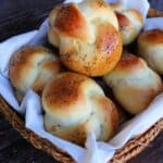 A linen lined basket full of poppy seed topped knotted challah rolls.