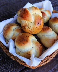 A linen lined basket full of poppy seed topped knotted challah rolls.