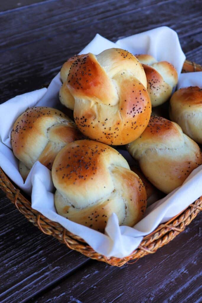 A linen lined basket full of knotted and seed topped challah rolls.