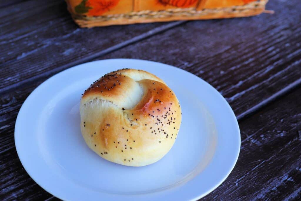 A poppy seed topped challah roll on a plate.