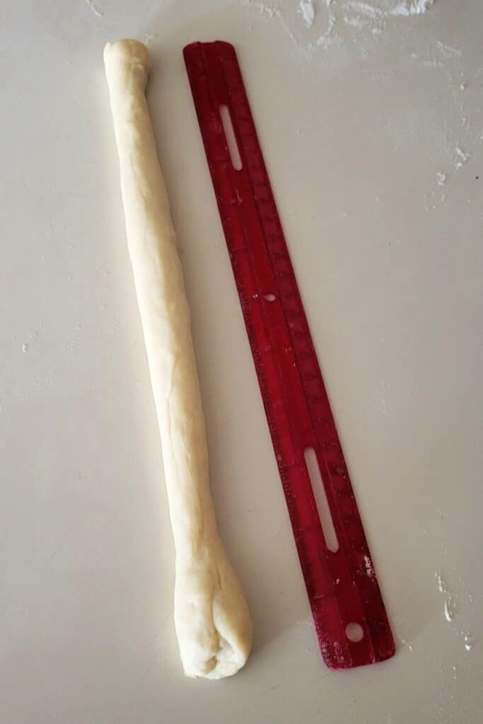 A rope of raw bread dough sits next to a red ruler.