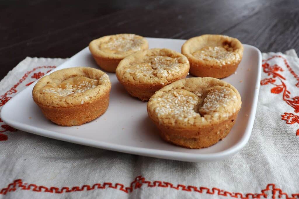 5 sesame seed topped mochi muffins sit on a plate.