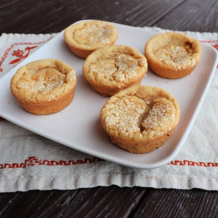 5 sesame seed topped mochi muffins on a square plate.