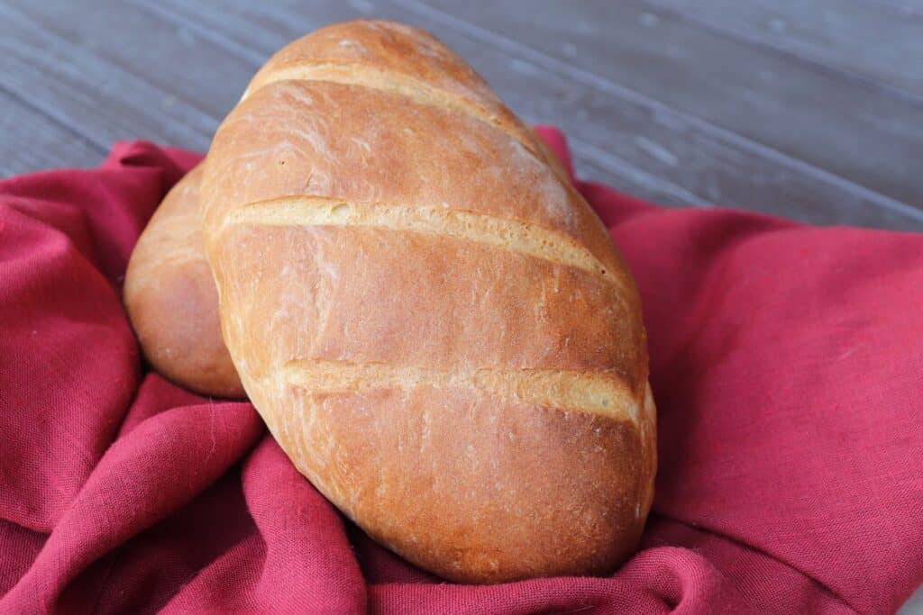 A loaf of Italian Bread sits on a red cloth.