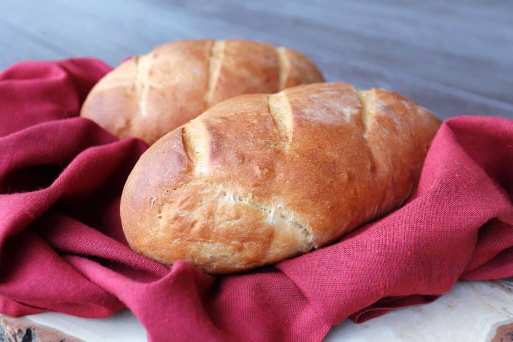 Two loaves of Italian bread sit wrapped in a red cloth on a board.