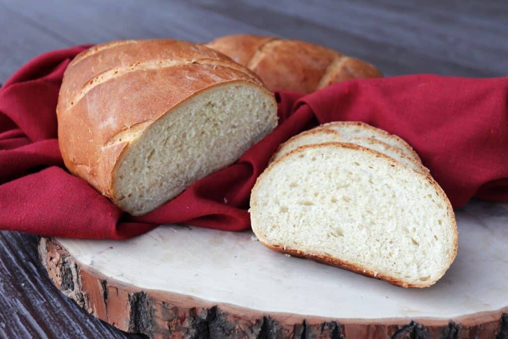 Slices of white bread sit on a board with the remaining loaf wrapped in a red cloth in the background.