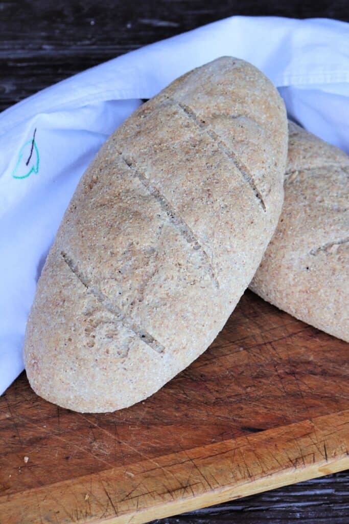 Close up of a loaf of whole wheat Italian bread sitting at an angle on top of another loaf. 