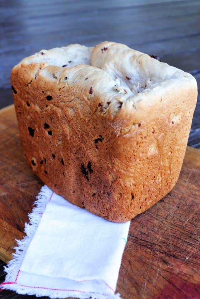 A loaf of cranberry walnut bread sits on top of a cloth napkin draped over a cutting board. 