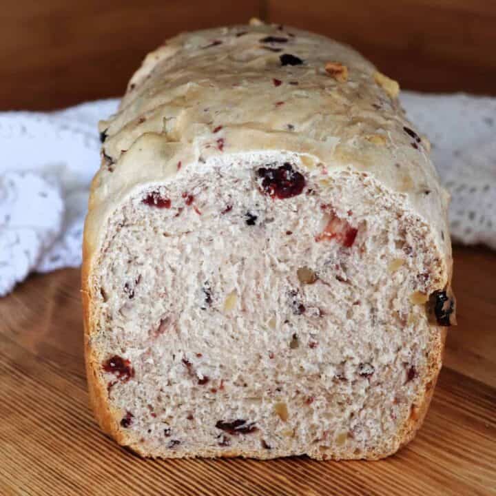 A loaf of cranberry walnut bread with the end cut off exposing the inside sits on a board.