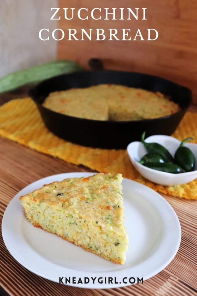 A piece of cornbread sits on a plate. A cast iron pan full of remaining cornbread sits in the background. Text overlay reads: zucchini cornbread.