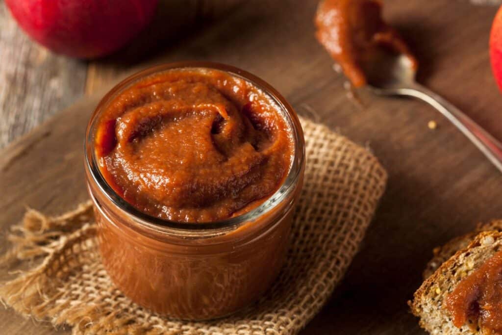 An open jar of apple butter sits on a piece of burlap as seen from above.