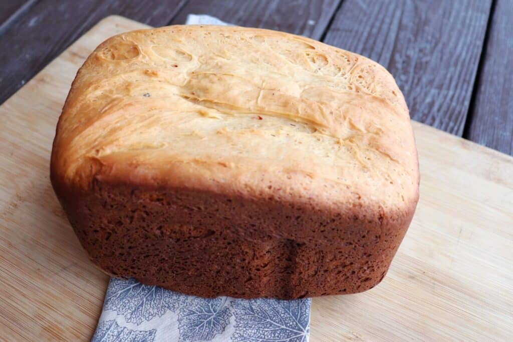 A loaf of bread machine cheese bread sits on a cloth draped board. 