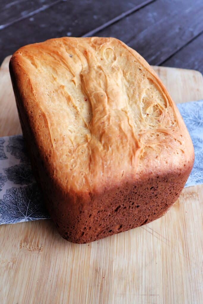 A loaf of bread machine cheese bread sits on a cloth draped board. 