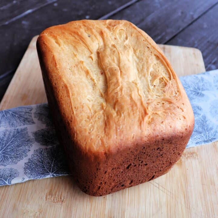 A loaf of bread machine cheese bread sits on a cloth draped board.