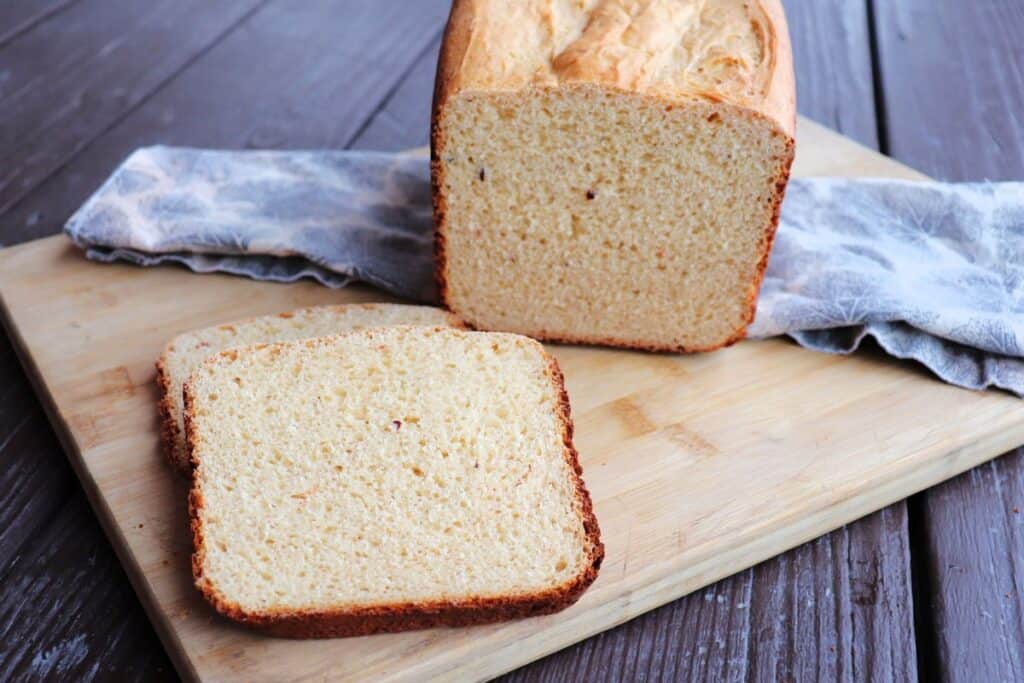 Slices of cheese bread sit on a board with the remaining loaf sitting behind them on a cloth.