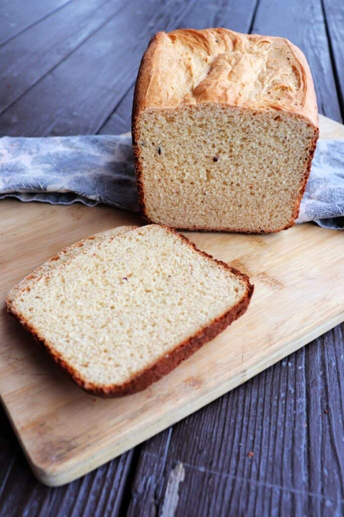 Slices of cheese bread sit on a board with the remaining loaf sitting behind them on a cloth.