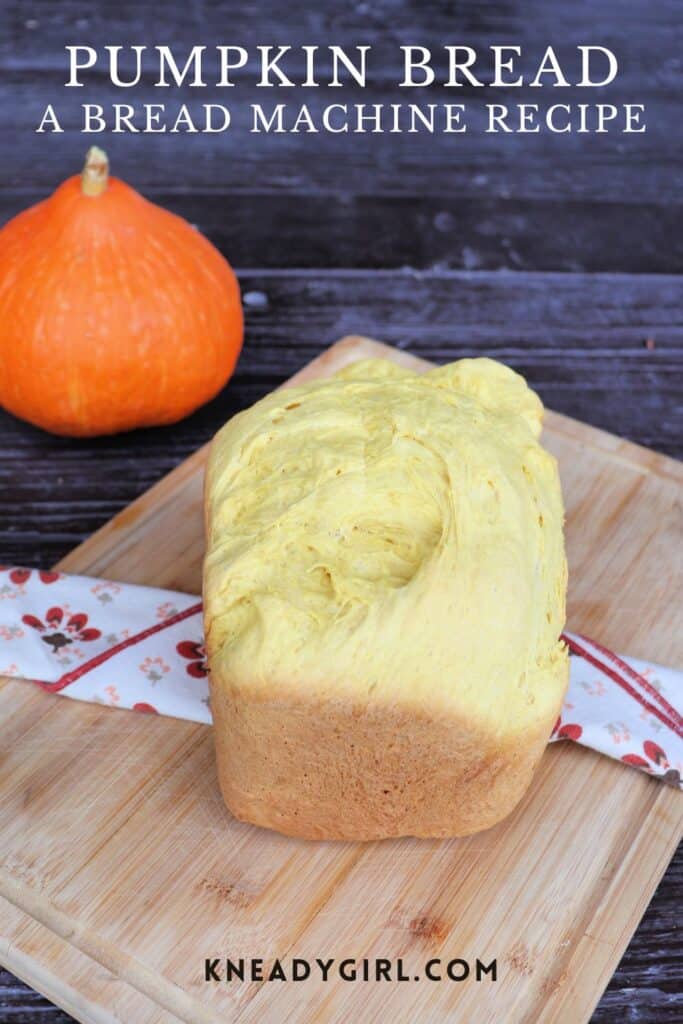 A loaf of bread sits on a cloth draped board with a fresh pumpkin in the background. Text overlay reads: Pumpkin Bread: A Bread Machine Recipe. 