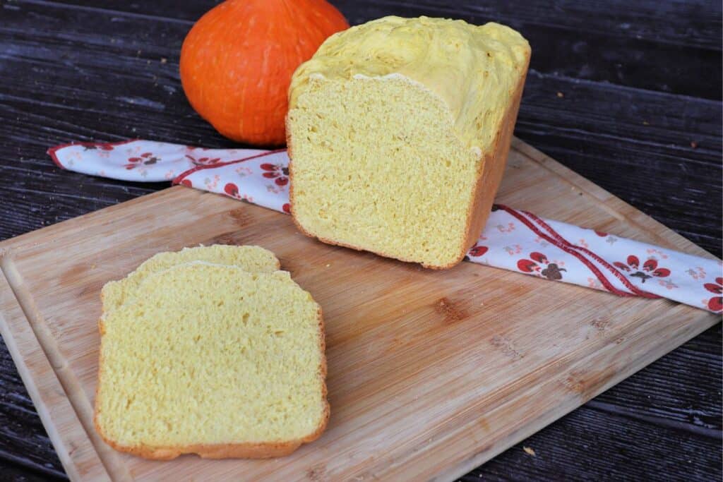 Slices of bread sit on a cutting board with remaining loaf behind it. A fresh pumpkin sits in the background. 