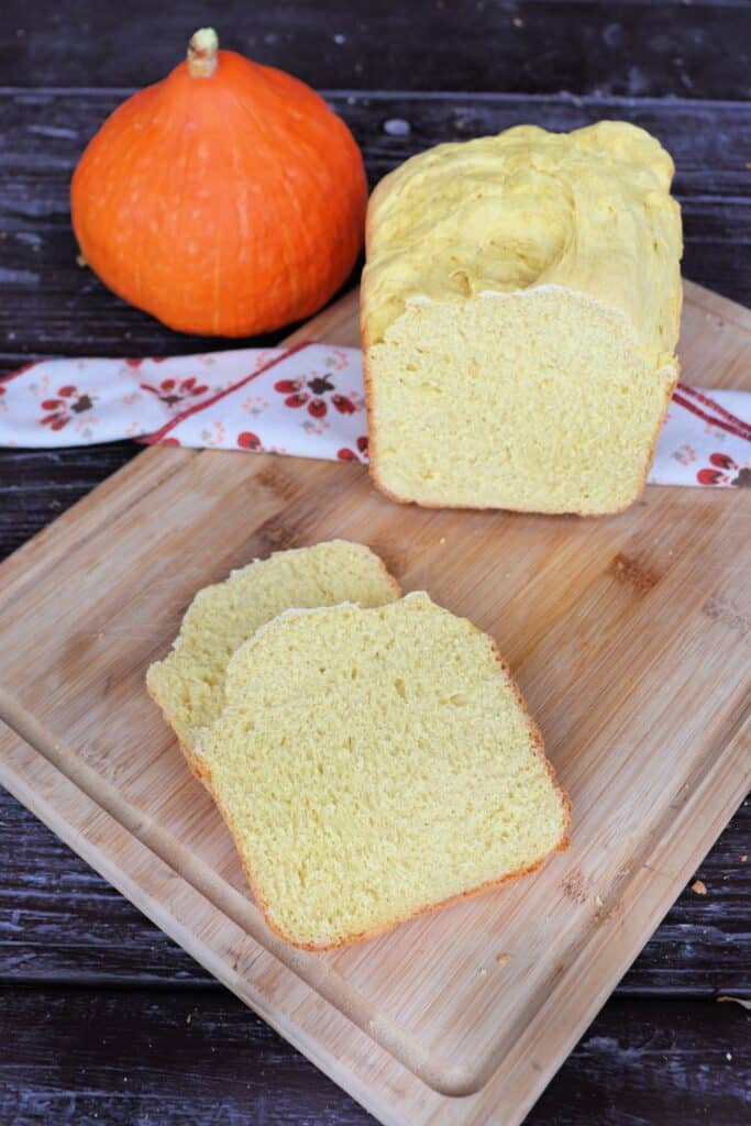 Slices of bread sit on a cutting board with remaining loaf behind it. A fresh pumpkin sits in the background. 