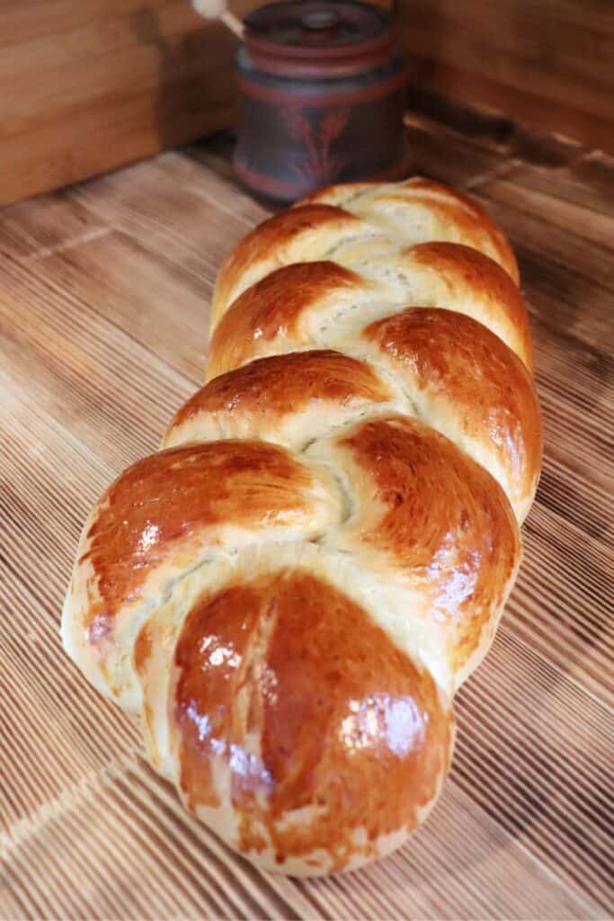 A loaf of Swiss bread sits on a board, a honey pot in the background. 