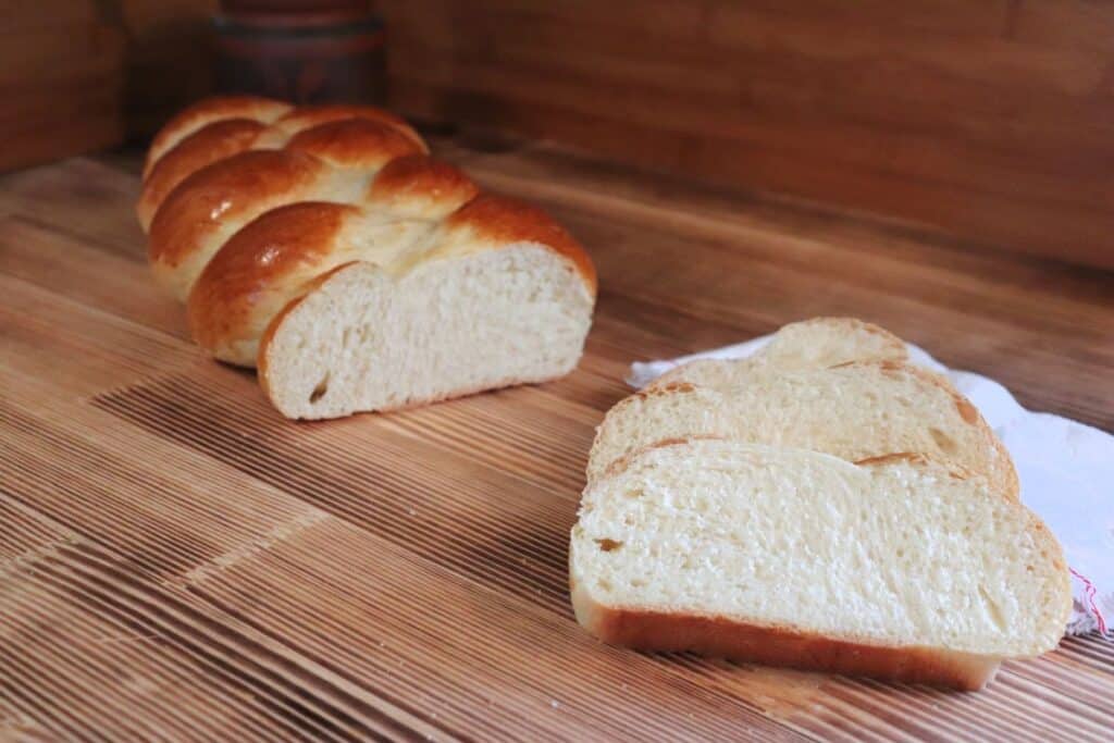 Slices of Zopf bread sit on a board with the remaining loaf behind them. 