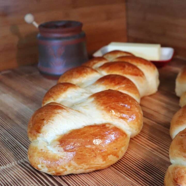 A loaf of swiss bread sits on a board, a honey pot and butter dish in the background.