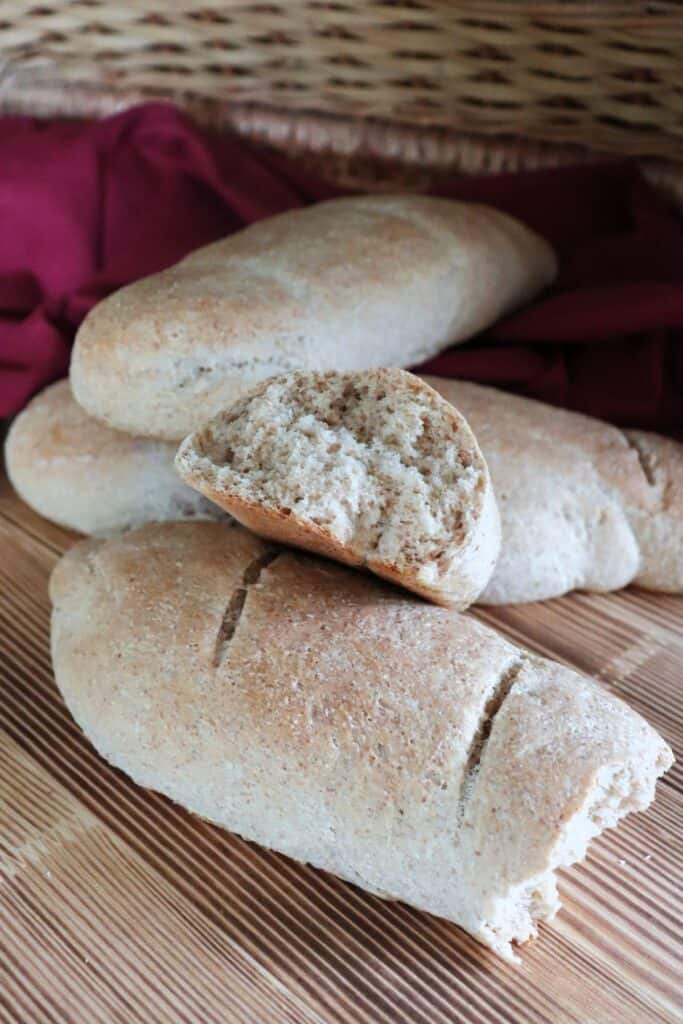 The end of a loaf of bread that has been torn exposing the inside sits on top of more loaves of bread. 