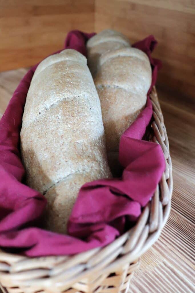 3 whole wheat baguettes stacked in a red cloth lined basket. 