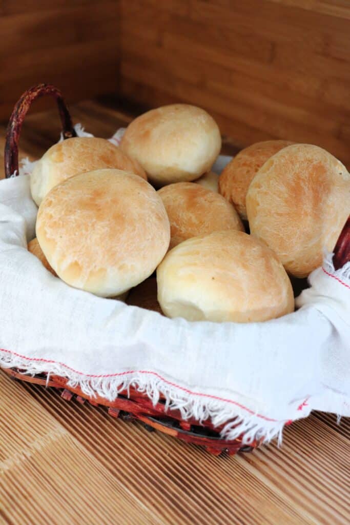 Dinner rolls stacked inside a cloth lined basket sit on a table. 