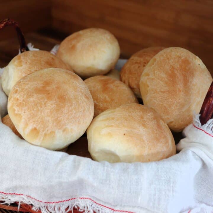 Dinner rolls stacked in a white cloth lined basket.