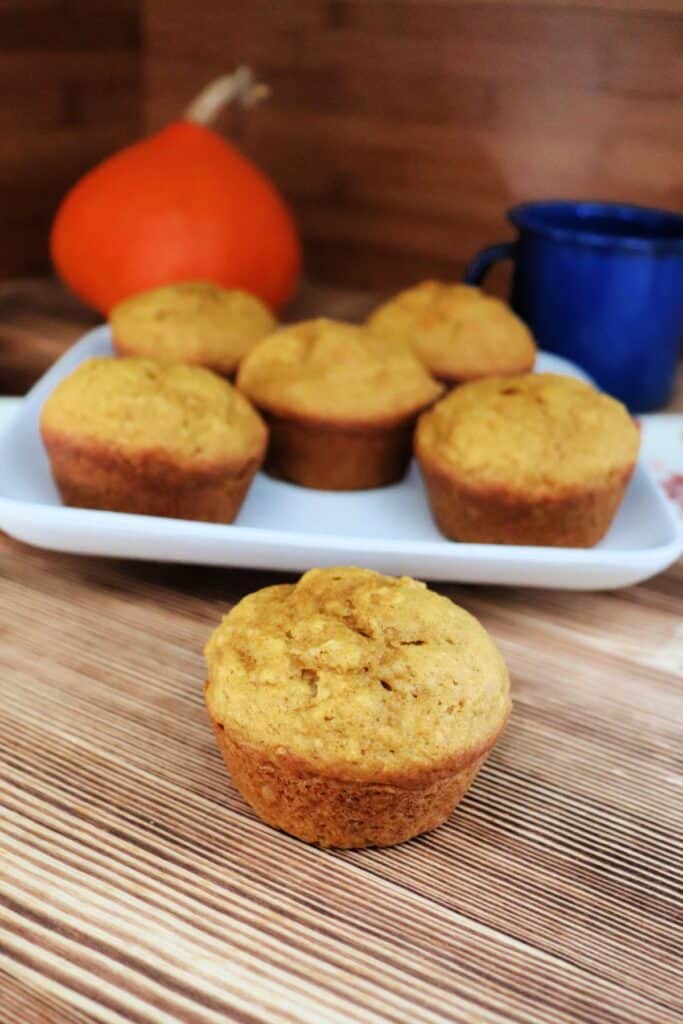A single muffin sits on a board with a plate of more muffins behind it. 