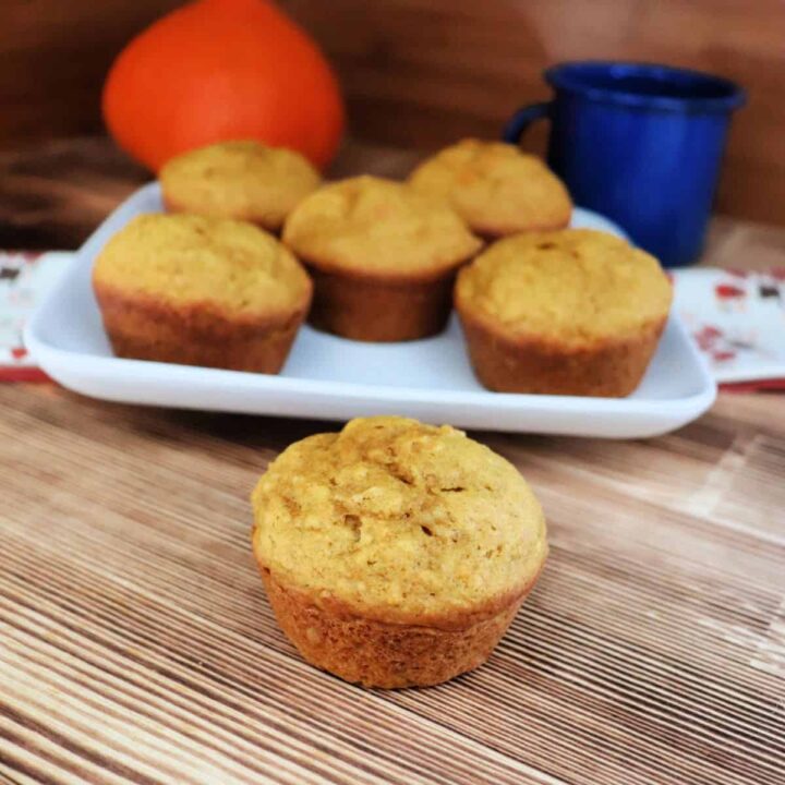 A single muffin sits on a board with a plate of more muffins behind it.