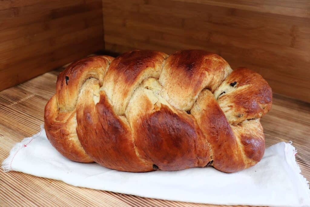 A braid loaf of bread sits on its side on a white napkin.