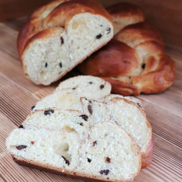 Slices of cinnamon raisin challah sit on a board with remaining loaf in the background.
