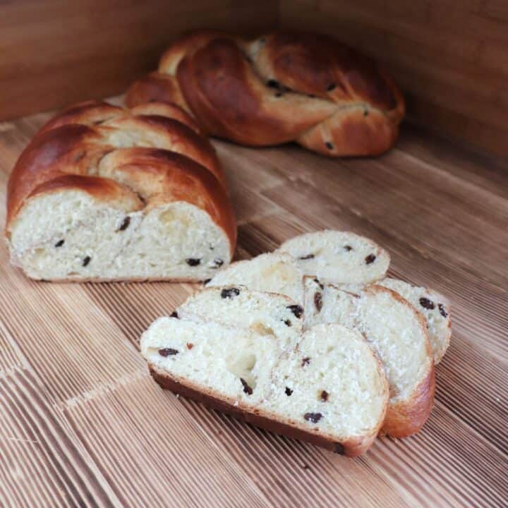 Slices of cinnamon raisin challah sit on a board with remaining loaf in the background.
