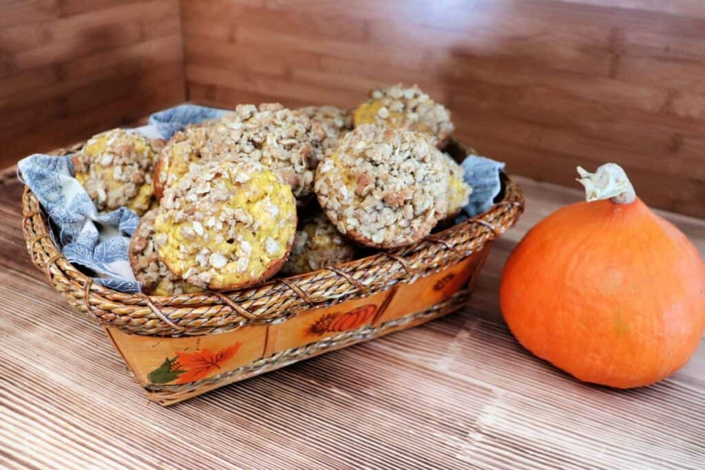 A basket of muffins sits on a board with a pumpkin next to it. 