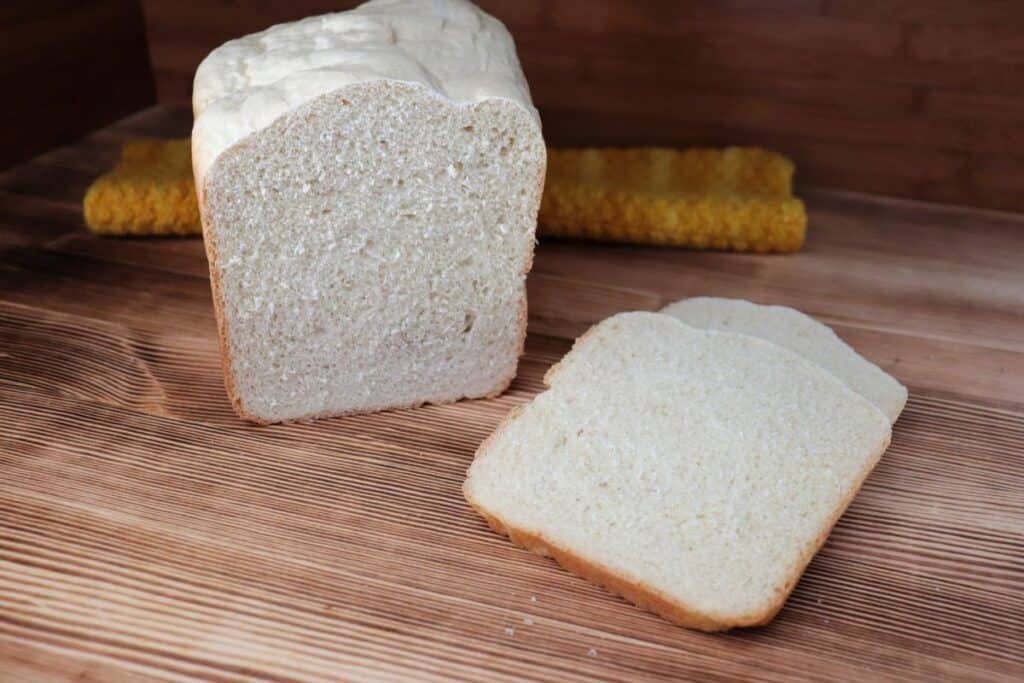 Slices of white bread sit on a board with remaining loaf behind them. 