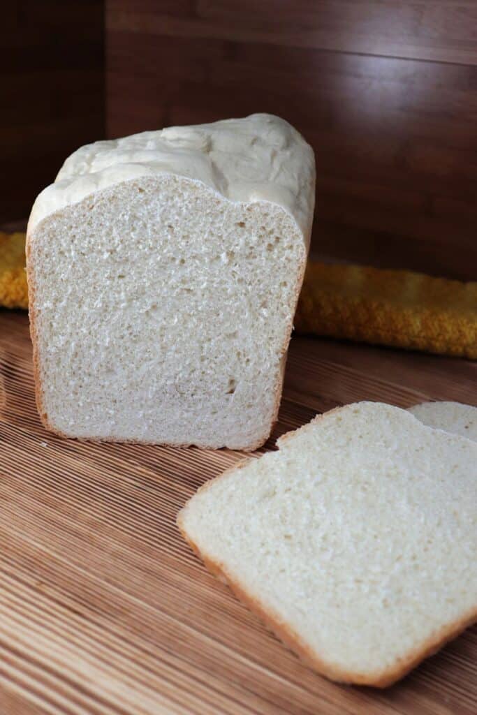A loaf of white bread sits on a board, slices of the loaf sit in front of it. 