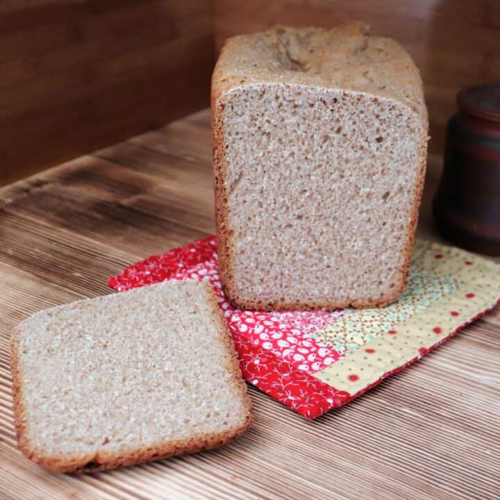 A slice of bread sits on a board with the remaining loaf behind it on a colorful pot holder.
