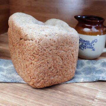 A loaf of bread sits on a piece of cloth with an earthenware pitcher in the background.