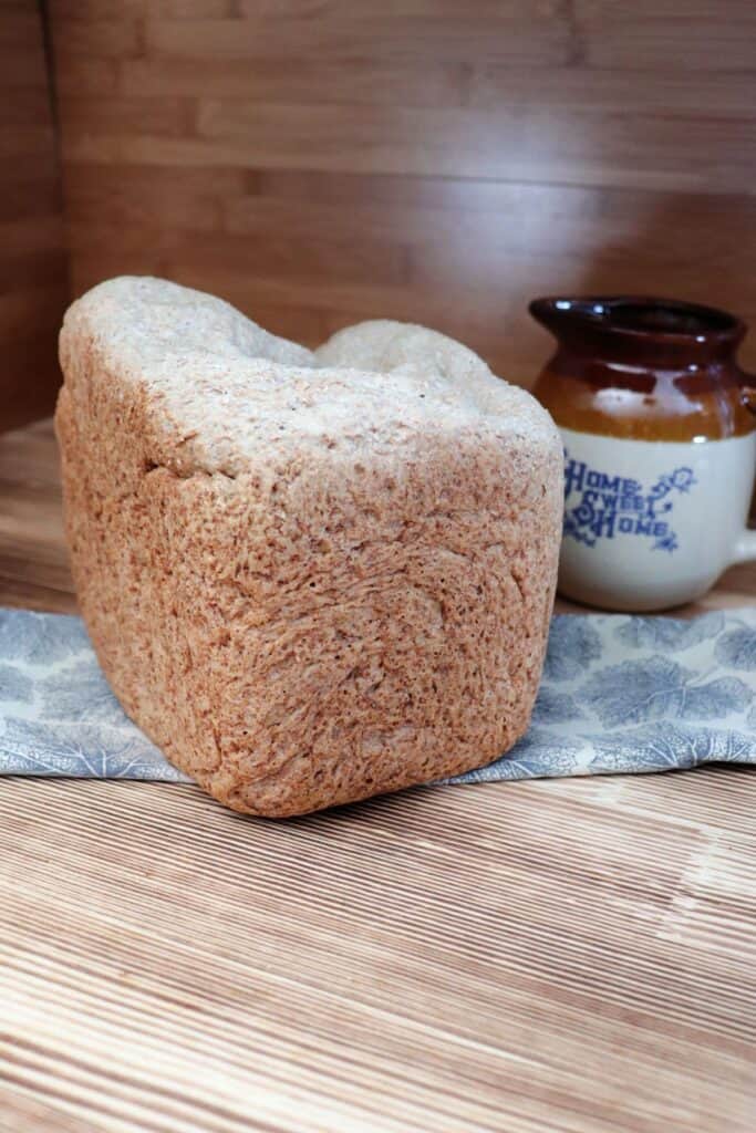 A loaf of bread sits on a piece of cloth with an earthenware pitcher in the background.