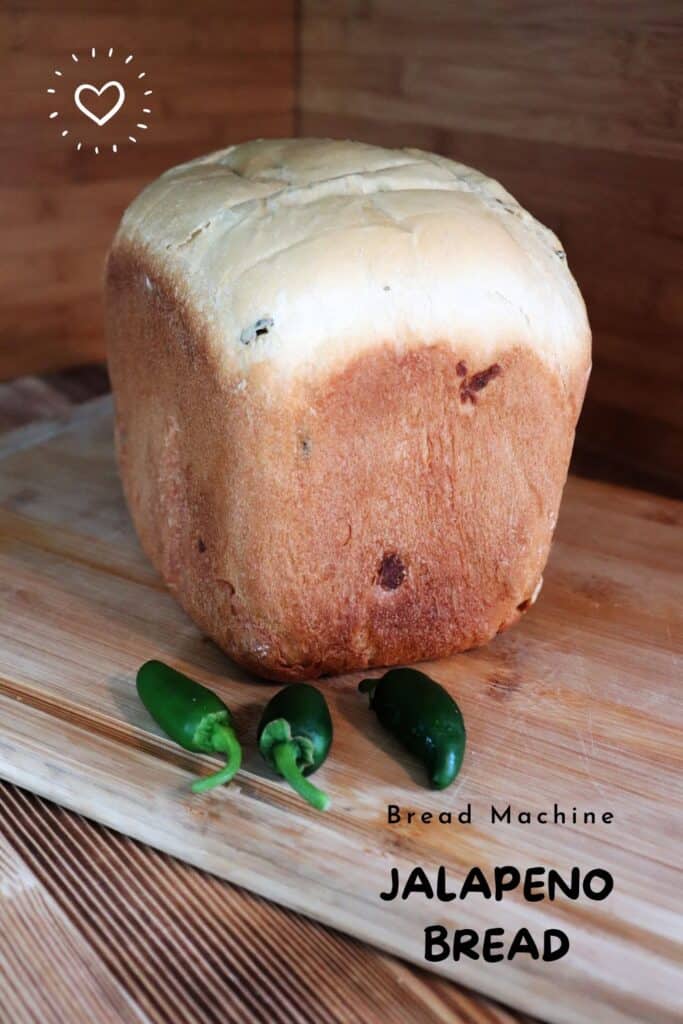 A loaf of bread sits on a board with some fresh jalapeno peppers in front of it. Text overlay reads: Bread Machine Jalapeno Bread.