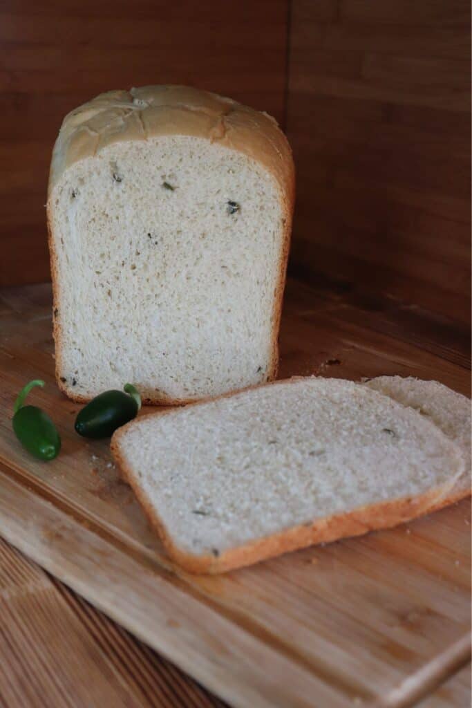 Slices of bread sit on a cutting board with remaining loaf and fresh jalapenos in the background. 