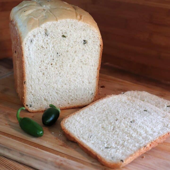 Slices ob bread sit on a board with remaining loaf and fresh jalapenos in the background.